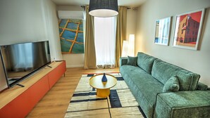 Una sala de estar moderna con una televisión de pantalla plana, un sofá verde, una mesa de centro redonda y un ventanal con cortinas.