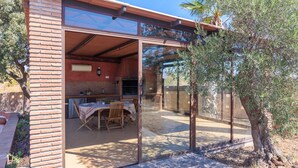 A patio area with a brick wall, a table with chairs, and a glass enclosure. - Villa Tinahones Álora by Ruralidays (Málaga)