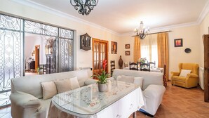 Uma sala de estar com sofá, mesa de centro de vidro com estampas florais, poltrona amarela e área de jantar com mesa e cadeiras.