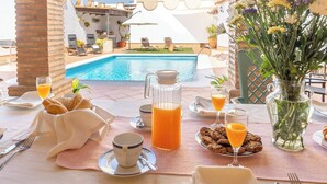 Disposição para o pequeno-almoço com vista para a piscina, incluindo uma mesa com alimentos, bebidas e um vaso de flores.