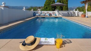 A pool area with a clear view of the mountains, a lounge chair, a sun hat, and a towel with a logo. - Casa La Paz - TRCP115 Torrox by Ruralidays (Málaga)