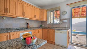 A kitchen with wooden cabinets, a granite countertop, a dishwasher, and a window with a view of the sea. - Casa La Paz - TRCP115 Torrox by Ruralidays (Málaga)