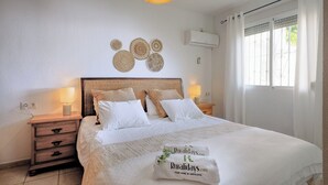 A neatly arranged bedroom with a bed, bedside tables, a wall-mounted air conditioner, and a window with curtains. - Casa La Paz - TRCP115 Torrox by Ruralidays (Málaga)