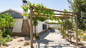 A covered outdoor area with a pergola, a stone wall, and a building with a tiled roof. - Villa Rosales Villanueva de la Concepción by Ruralidays (Málaga)