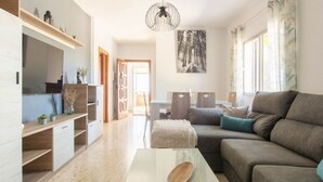A modern living room with a sofa, coffee table, and a dining area with chairs. There is a bookshelf and a painting on the wall. - Villa Rosales Villanueva de la Concepción by Ruralidays (Málaga)