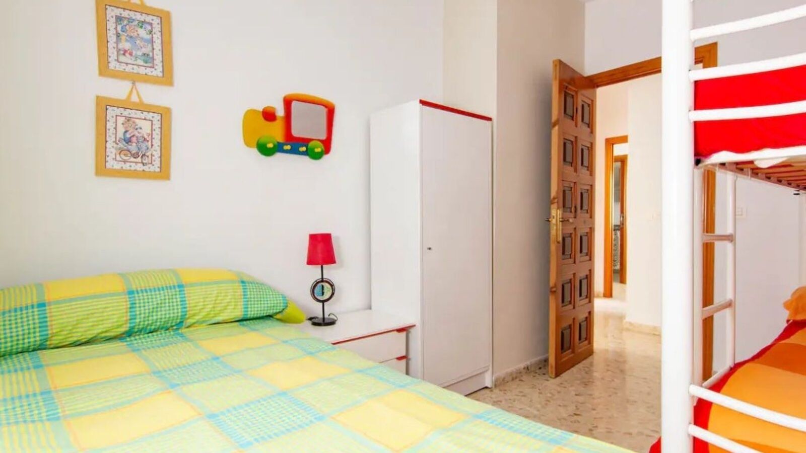Een slaapkamer met een bed, een garderobe, een rode lamp en een deur naar een andere kamer.