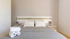 A neatly made bed with a grey bedspread and two white pillows, a folded towel on the left side, and a bedside table with a lamp and a phone on the right. - Villa Rosales Villanueva de la Concepción by Ruralidays (Málaga)
