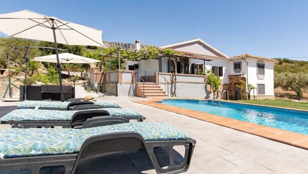 A poolside area with lounge chairs, a pool, and a house with a patio. - Villa Rosales Villanueva de la Concepción by Ruralidays (Málaga)