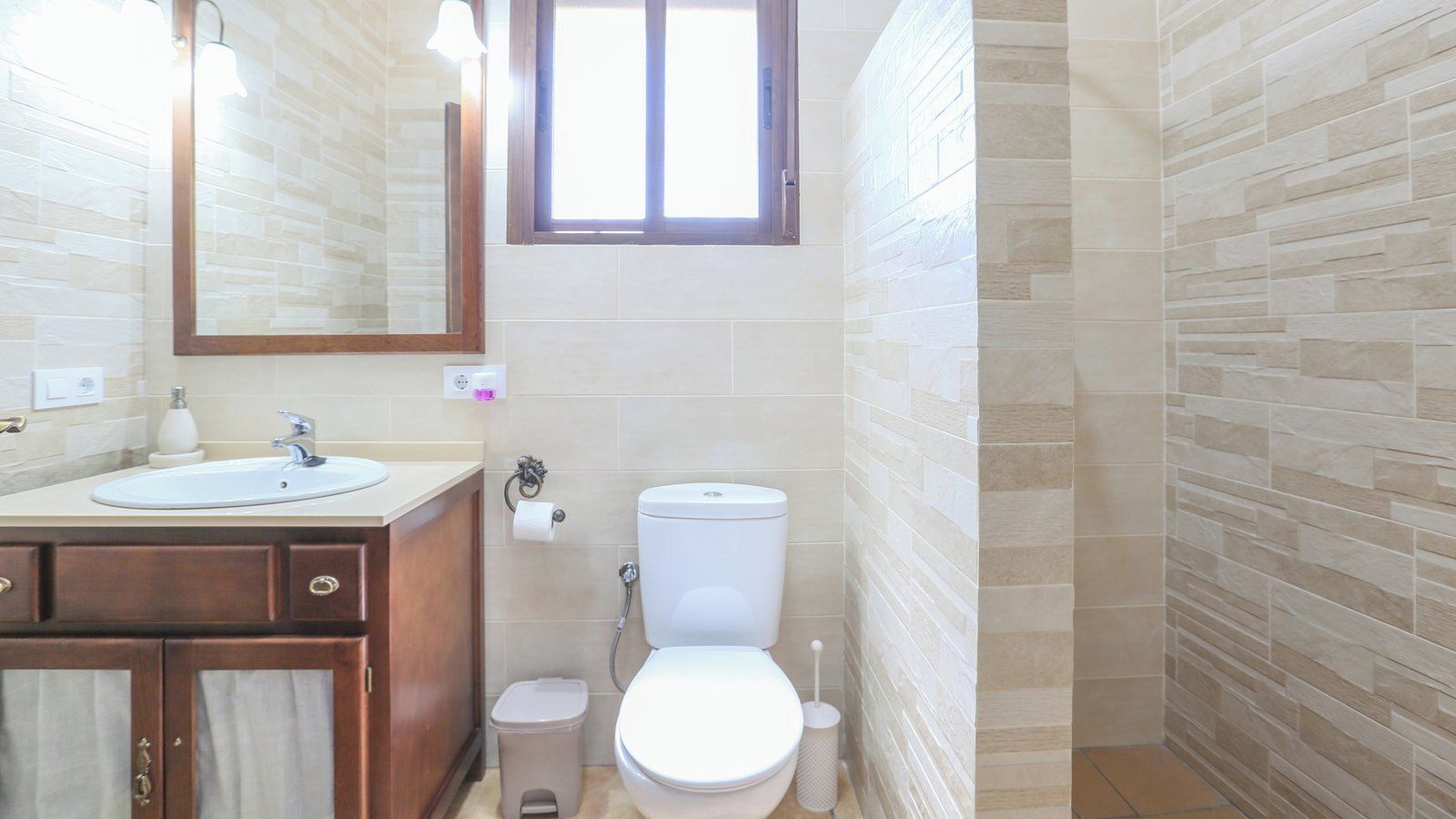 A bathroom with a sink, mirror, toilet, and a window.