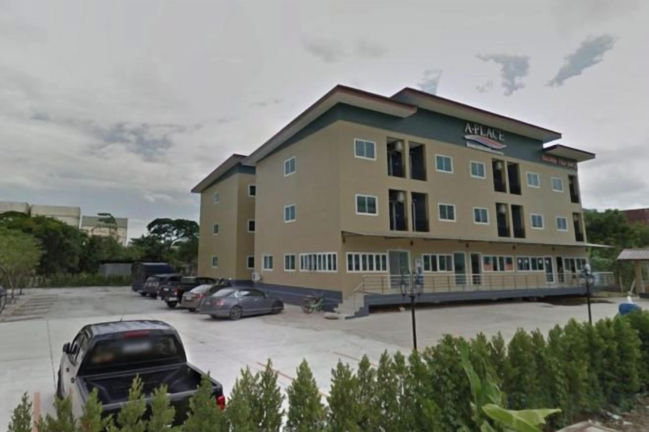 Un hotel a più piani con tetto piatto, un parcheggio e alcune auto parcheggiate.