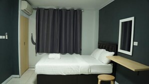 A bedroom with a bed, a bedside table, a small stool, a wall-mounted TV, and a window with curtains. - A-Place Suvarnabhumi (Bang Phli)