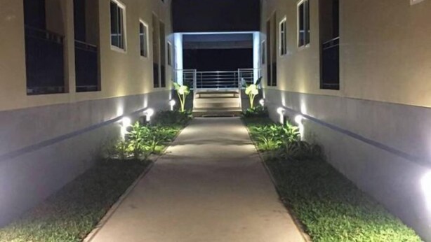 A corridor with a central pathway flanked by greenery and illuminated by wall-mounted lights. - A-Place Suvarnabhumi (Bang Phli)
