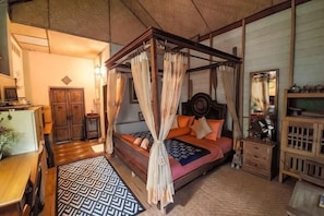 A four-poster bed with a canopy, a wooden nightstand, a mirror, and a patterned rug.