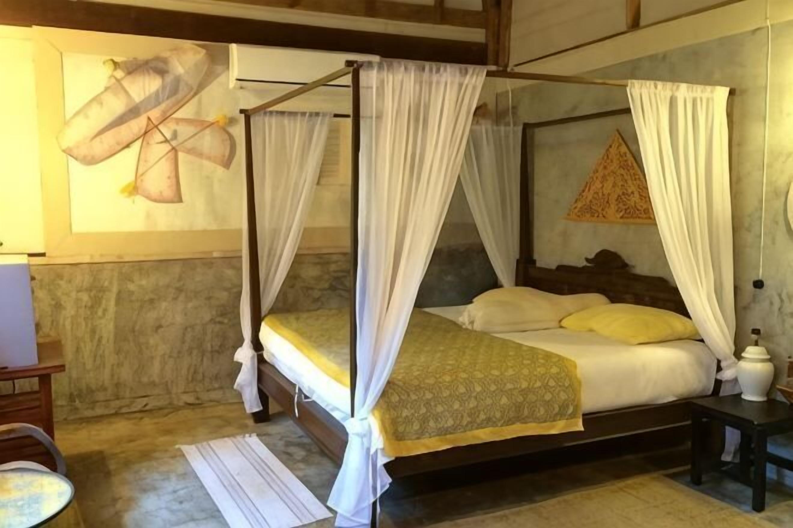 A four-poster bed with white drapes, a wooden headboard, and a patterned bedspread.