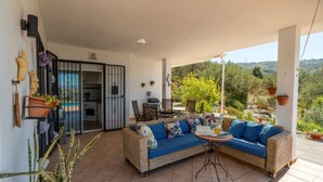 A covered outdoor seating area with a wicker sofa and a small table, surrounded by potted plants and a view of the landscape. - Casa Hermanas Alcaucín by Ruralidays (Málaga)