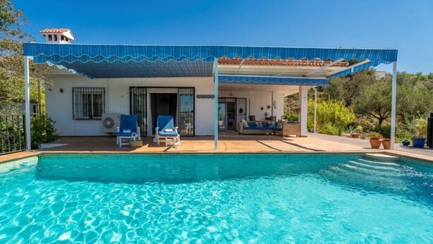 A poolside area with a covered seating area, a pool, and a building with a tiled roof. - Casa Hermanas Alcaucín by Ruralidays (Málaga)