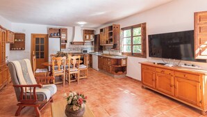 Amplia sala de estar con comedor, armarios de madera, televisor y área de cocina con ventana.