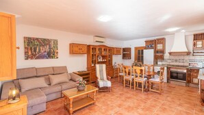 Una sala de estar acogedora con sofá, una mesa de centro y un comedor con sillas de madera. Se observa una cocina con estufa y alacenas.