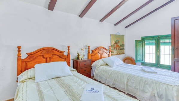 Un dormitorio con dos camas de madera, una mesita de noche, un cuadro y una ventana con contraventanas verdes.