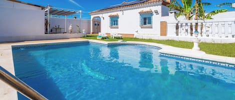 A swimming pool with a clear blue water, surrounded by a white building with blue windows and a white fence.