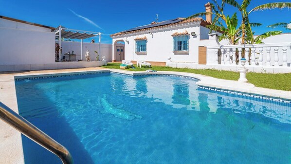 Una piscina amb aigua transparent i de color blau, envoltada d'un edifici blanc amb finestres blaves i una tanca blanca.
