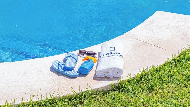 Et område ved poolen med et håndklæde, flip-flops, solbriller og solcreme.