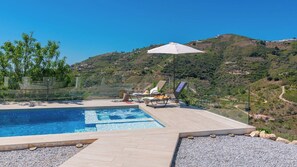 A swimming pool with lounge chairs and an umbrella, surrounded by a pebble beach and overlooking a hilly landscape. - Villa Serena Cómpeta by Ruralidays (Málaga)