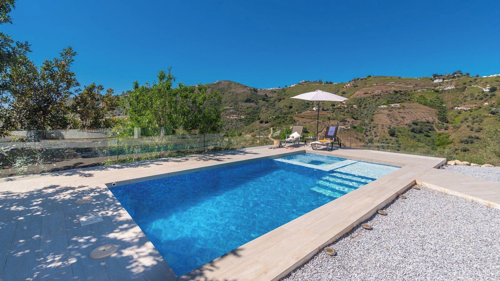 Una piscina rettangolare con acqua cristallina, circondata da una spiaggia di ciottoli e un pontile in legno.