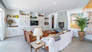 A living room with a sofa, coffee table, and TV. There are cabinets with decorative items and a plant. - Finca Naveda Barbate by Ruralidays (Cádiz)