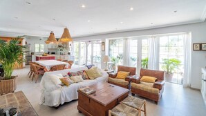 A spacious living area with a sofa set, a wooden coffee table, and wicker chairs. There is a dining area with a table and chairs, and a kitchen in the background. - Finca Naveda Barbate by Ruralidays (Cádiz)