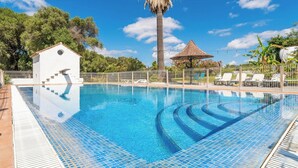 A swimming pool with clear blue water, surrounded by a white fence, a palm tree, and a small white building. - Finca Naveda Barbate by Ruralidays (Cádiz)