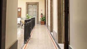 Un couloir au sol carrelé, un balcon orné d’une balustrade en fer forgé et une porte sur laquelle est apposée une enseigne.