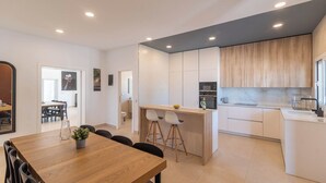 Una cocina moderna con armarios blancos, una isla de madera y un comedor con mesa y sillas de madera.