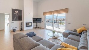 Amplia sala de estar con un amplio sofá, televisor y vistas al exterior.