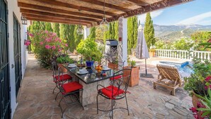 An outdoor patio with a stone floor, a wooden pergola, a table with chairs, and a pool.