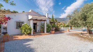 A white building with a tiled roof, a gravel driveway, and potted plants.