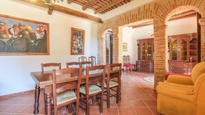 A dining area with a wooden table and chairs, a painting on the wall, and a red chair in the background. - Cortijo San Rafael Constantina by Ruralidays (Seville)