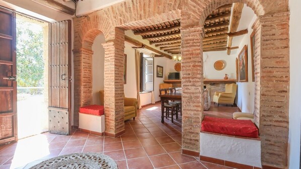 A spacious living area with exposed brick arches, a fireplace, and a dining area with wooden furniture. - Cortijo San Rafael Constantina by Ruralidays (Seville)