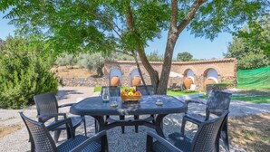 An outdoor dining area with a round table and chairs, surrounded by trees and a stone wall. - Cortijo San Rafael Constantina by Ruralidays (Seville)