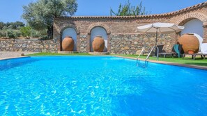 A swimming pool with stone walls and arched openings, surrounded by a grassy area and trees. - Cortijo San Rafael Constantina by Ruralidays (Seville)