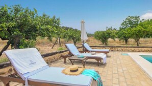 Zona de piscina con sillones reclinables y una pequeña mesa, rodeada de árboles y un cielo despejado.