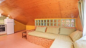 Una habitación acogedora con techo de madera, un sofá estampado en ladrillos, una mesita, un refrigerador y una zona de cocina con horno.
