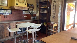 Una cucina rustica con zoccolo in mattoni, sgabelli da bar bianchi, un tavolo di legno e uno scaffale con bicchieri.