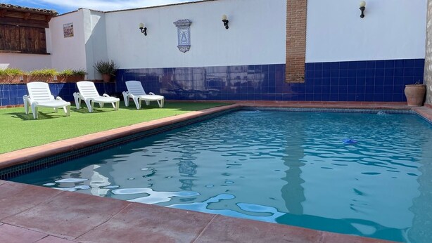 Una piscina con lettini bianchi e un muro rivestito di piastrelle.