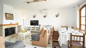 Una sala de estar con chimenea, sofá, televisor y comedor con mesa dispuesta para seis personas.