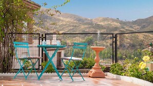 Un patio al aire libre con sillas plegables color turquesa y una mesa, una fuente de terracota y vistas a las montañas.