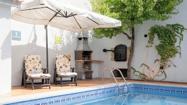 Zona junto a la piscina con dos sillas, una parrilla y un árbol.