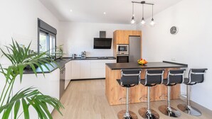 A modern kitchen with a central island, bar stools, and a wooden cabinet.