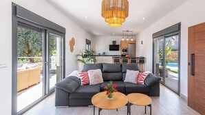A modern living room with a grey sofa, two round wooden tables, and a large window overlooking a garden.