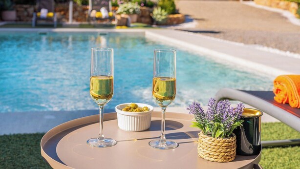 Two glasses of white wine on a round table with a bowl of olives and a basket of lavender.